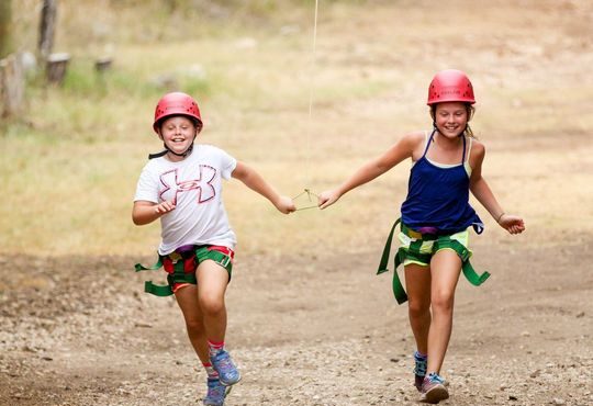 Two campers run together after finishing a ropes course at T Bar M Camp in Spicewood, Texas. (Photo...