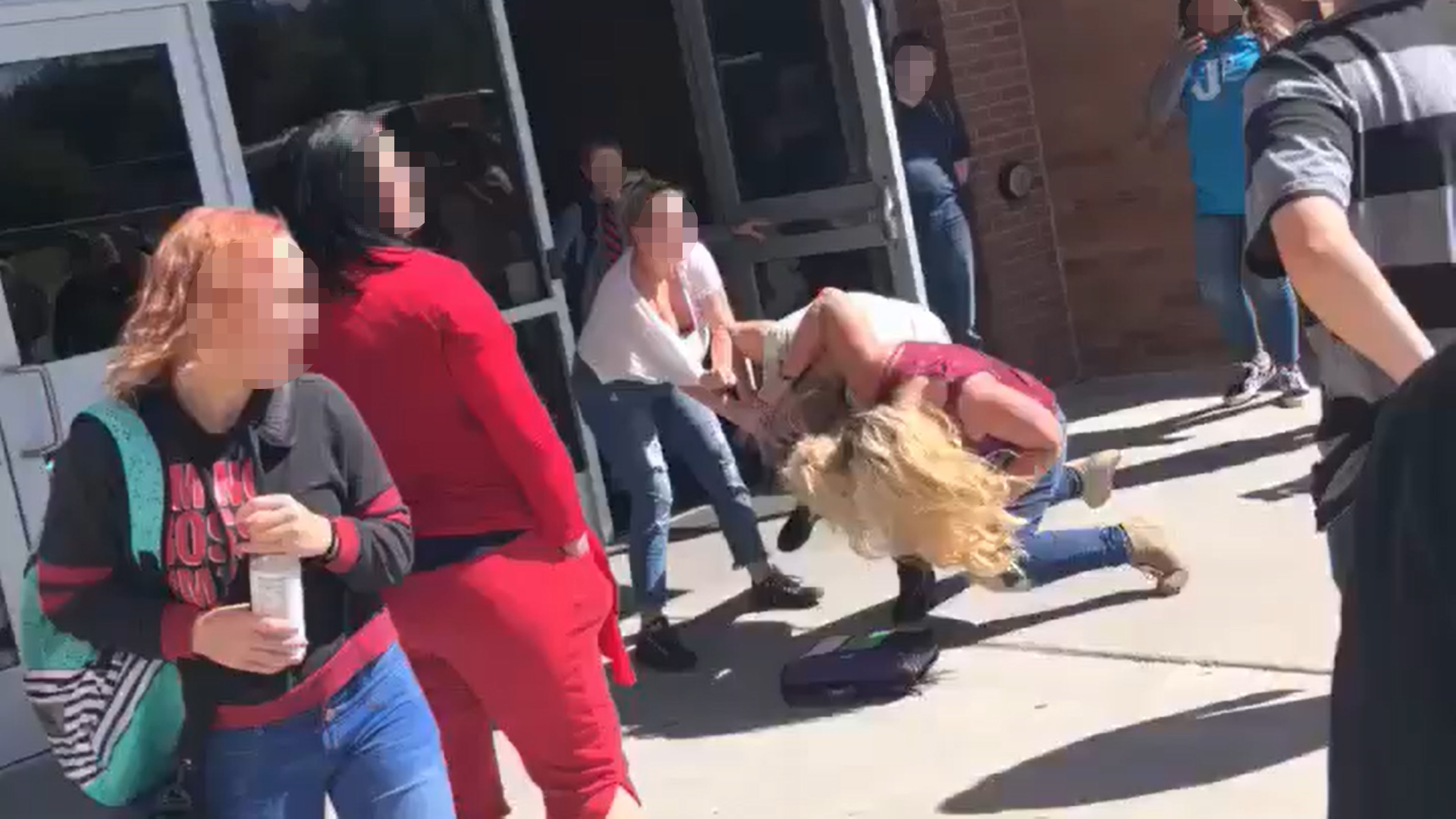 A woman in red, allegedly a teacher at the school, looks on during the assault. (Photo taken from video provided by Tonya Hiner)