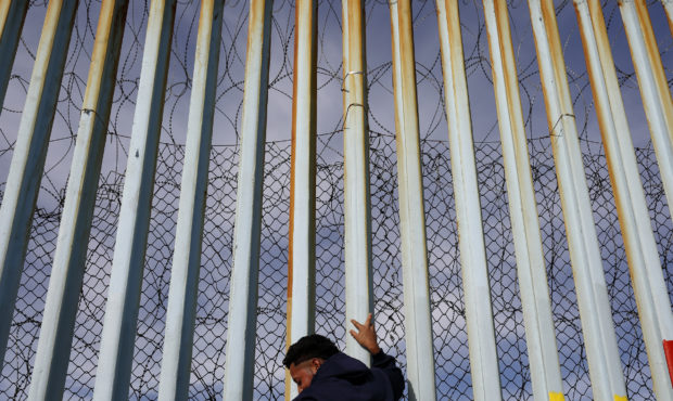 A man holds on to the border wall along the beach, Tuesday, Jan. 8, 2019, in Tijuana, Mexico. Ready...