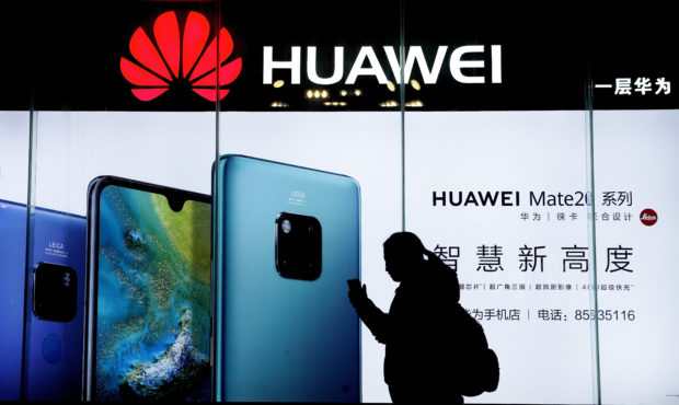 FILE - In this Dec. 11, 2018, file photo, a woman browses her smartphone as she walks by a Huawei s...