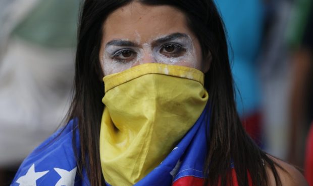 An anti-government protester covers her face with a Venezuelan flag, and uses toothpaste around her...