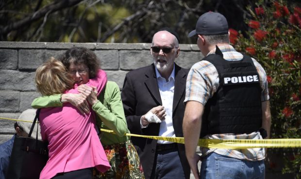 Two people hug as another talks to a San Diego County Sheriff's deputy outside of the Chabad of Pow...