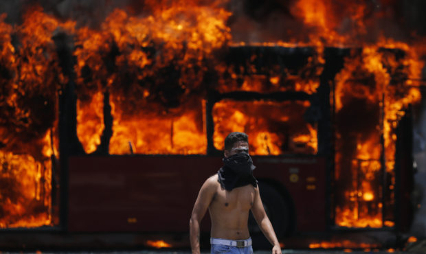 An anti-government protester walks near a bus that was set on fire by opponents of Venezuela's Pres...