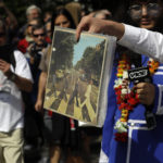 A fan carries a copy of the album 'Abbey Road' as he crosses the Abbey Road zebra crossing on the 50th anniversary of British pop musicians The Beatles doing it for their album cover of 'Abbey Road' in St Johns Wood in London, Thursday, Aug. 8, 2019. They aimed to cross 50 years to the minute since the 'Fab Four' were photographed for the album. (AP Photo/Kirsty Wigglesworth)