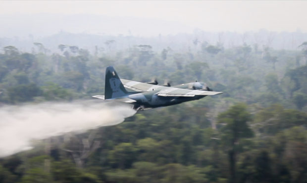 In this photo released by Brazil Ministry of Defense, a C-130 Hercules aircraft dumps water to figh...