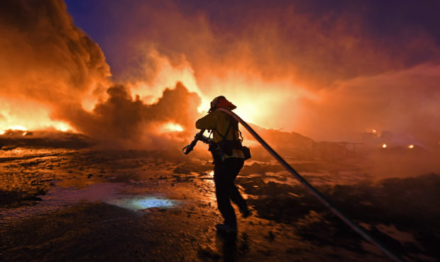 FILE - In this Oct. 27, 2019 file photo, a firefighter drags a hose closer to battle a grass fire o...