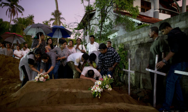 FILE - In this April 22, 2019, file photo, relatives place flowers after the burial of three victim...