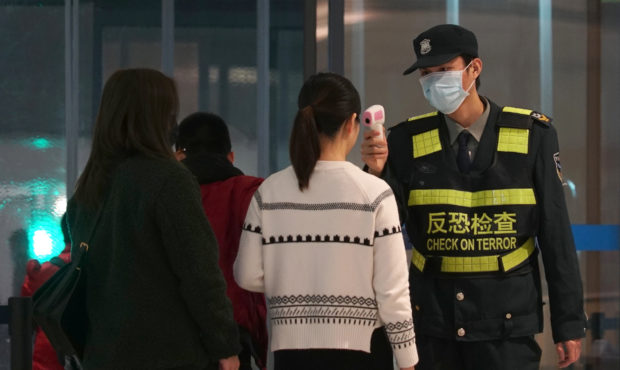 An airport staff member uses a temperature gun to check people leaving Wuhan Tianhe International A...