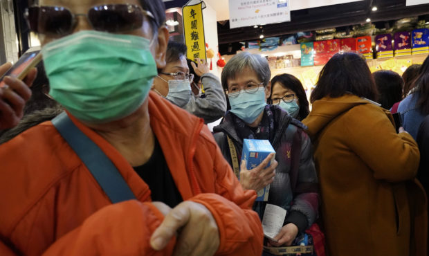 A woman holds a box of face mask as people queue up waiting to purchase face masks outside a shop i...