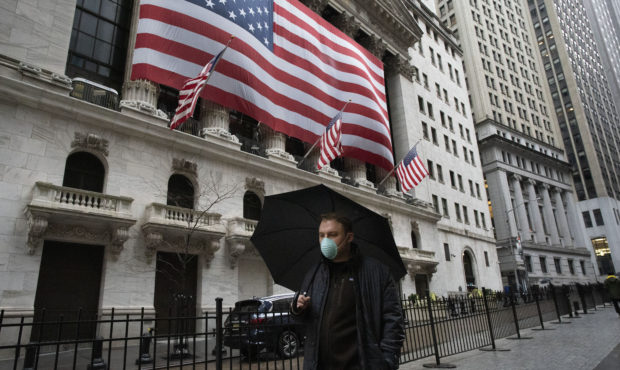 A man wearing a mask walks by the New York Stock Exchange, Tuesday, March 17, 2020. Share prices ar...