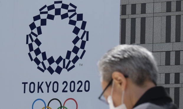 A man wearing a face mask walks before the logo of the Tokyo 2020 Olympic Games displayed on the To...