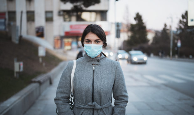 Portrait of young Latino woman with face mask on the street, looking at camera....