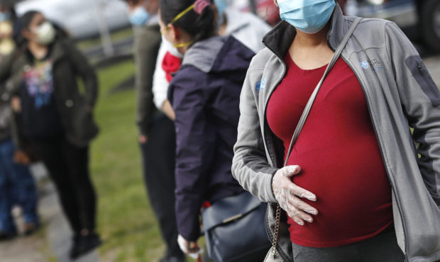 pregnant woman in line wearing mask COVID-19 vaccine...