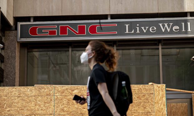 A pedestrian wearing a protective mask walks past a boarded up GNC store in Washington, D.C., U.S.,...