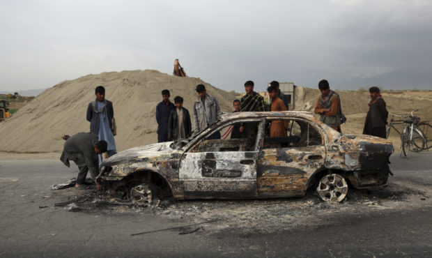 FILE - In this April 9, 2019, file photo, Afghans watch a civilian vehicle burnt after being shot b...