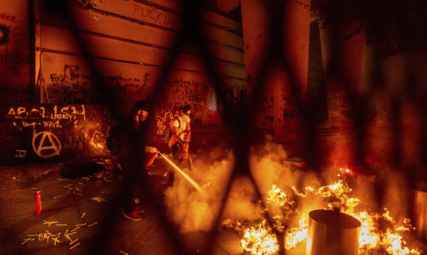 A protester extinguishes a fire set by fellow protesters at the Mark O. Hatfield United States Cour...