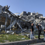 People stand in front of a destroyed building near the scene of an explosion that hit the seaport of Beirut, Lebanon, Wednesday, Aug. 5, 2020. A massive explosion rocked Beirut on Tuesday, flattening much of the city's port, damaging buildings across the capital and sending a giant mushroom cloud into the sky. (AP Photo/Bilal Hussein)