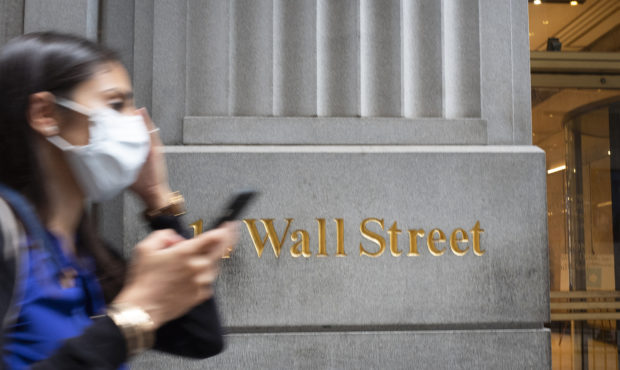 FILE - In this June 30, 2020 file photo, a woman wearing a mask passes a sign for Wall Street durin...