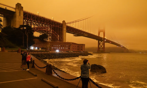 People stop at Fort Point to take morning pictures of the Golden Gate Bridge covered in smoke from ...