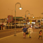 Under darkened skies from wildfire smoke, people walk at Fisherman's Wharf Wednesday, Sept. 9, 2020, in San Francisco. People from San Francisco to Seattle woke Wednesday to hazy clouds of smoke lingering in the air, darkening the sky to an eerie orange glow that kept street lights illuminated into midday, all thanks to dozens of wildfires throughout the West. The picture was taken in the middle of the day at 1:01 p.m. (AP Photo/Eric Risberg)