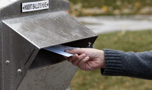 A person's hand is photographed dropping a ballot into a Utah drop box....