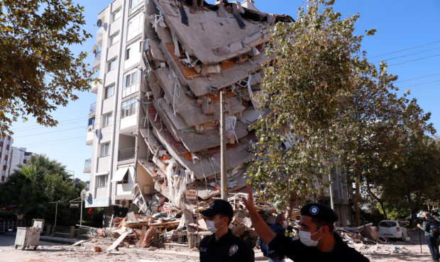 Members of security officers walk by the debris of a collapsed building in Izmir, Turkey, Saturday,...