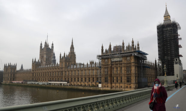 A woman wearing a face mask, walks across Westminster Bridge past the Houses of Parliament in Londo...