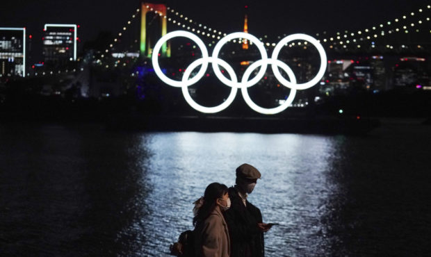 FILE - In this Dec. 1, 2020, file photo, a man and a woman walk past near the Olympic rings floatin...