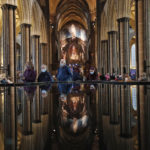 People are reflected in the 'Refection Pool' inside Salisbury Cathedral in Salisbury, England, Wednesday, Jan. 20, 2021, as they leave after receiving their Pfizer-BioNTech vaccination. Salisbury Cathedral opened its doors for the second time as a venue for the Sarum South Primary Care Network COVID-19 Local Vaccination Service. (AP Photo/Frank Augstein)