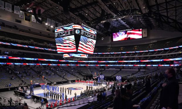 The Dallas Mavericks and Atlanta Hawks, along with a limited fan attendance, stand during the playi...