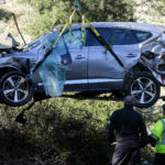 Workers watch as a crane is used to lift a vehicle following a rollover accident involving golfer Tiger Woods, Tuesday, Feb. 23, 2021, in the Rancho Palos Verdes section of Los Angeles. Woods suffered leg injuries in the one-car accident and was undergoing surgery, authorities and his manager said. (AP Photo/Ringo H.W. Chiu)