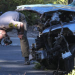 A law enforcement officer looks over a damaged vehicle following a rollover accident involving golfer Tiger Woods, Tuesday, Feb. 23, 2021, in the Rancho Palos Verdes suburb of Los Angeles. Woods suffered leg injuries in the one-car accident and was undergoing surgery, authorities and his manager said. (AP Photo/Ringo H.W. Chiu)