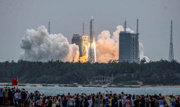 TOPSHOT - People watch a Long March 5B rocket, carrying China's Tianhe space station core module, a...