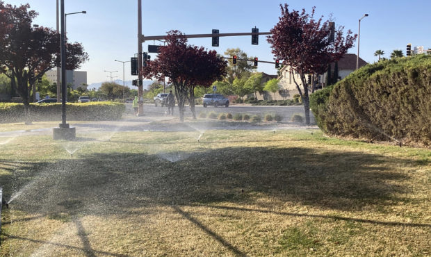 FILE - In this April 9, 2021, file photo, sprinklers water grass near a street corner in the Summer...