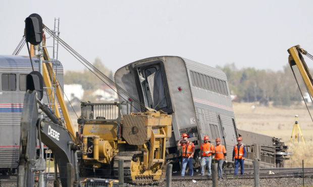 Workers walk Sunday, Sept. 26, 2021, next to an Amtrak train that derailed Saturday just west of Jo...
