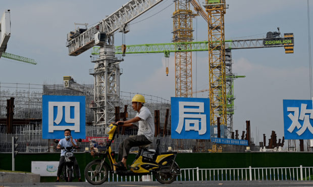 Workers drive their motorbikes in front of the under-construction Guangzhou Evergrande football sta...