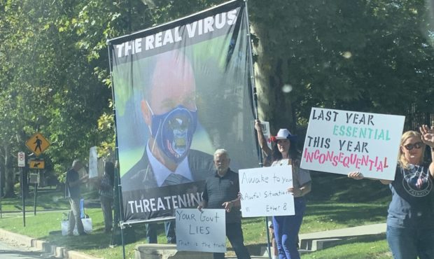 Anti-vaccine demonstrators hold a large banner with a photo of Utah Gov. Spencer Cox referring to h...