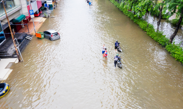 Image of severe flooding with people wading through water in the street. Photo credit: Canva...