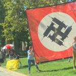 Anti-vaccine demonstrators displayed a large banner fashioned after a Nazi flag and featuring a swastika made out of vaccine syringes during a protest at the Utah Governor's Mansion in Salt Lake City on Sunday. (Bri Bright)