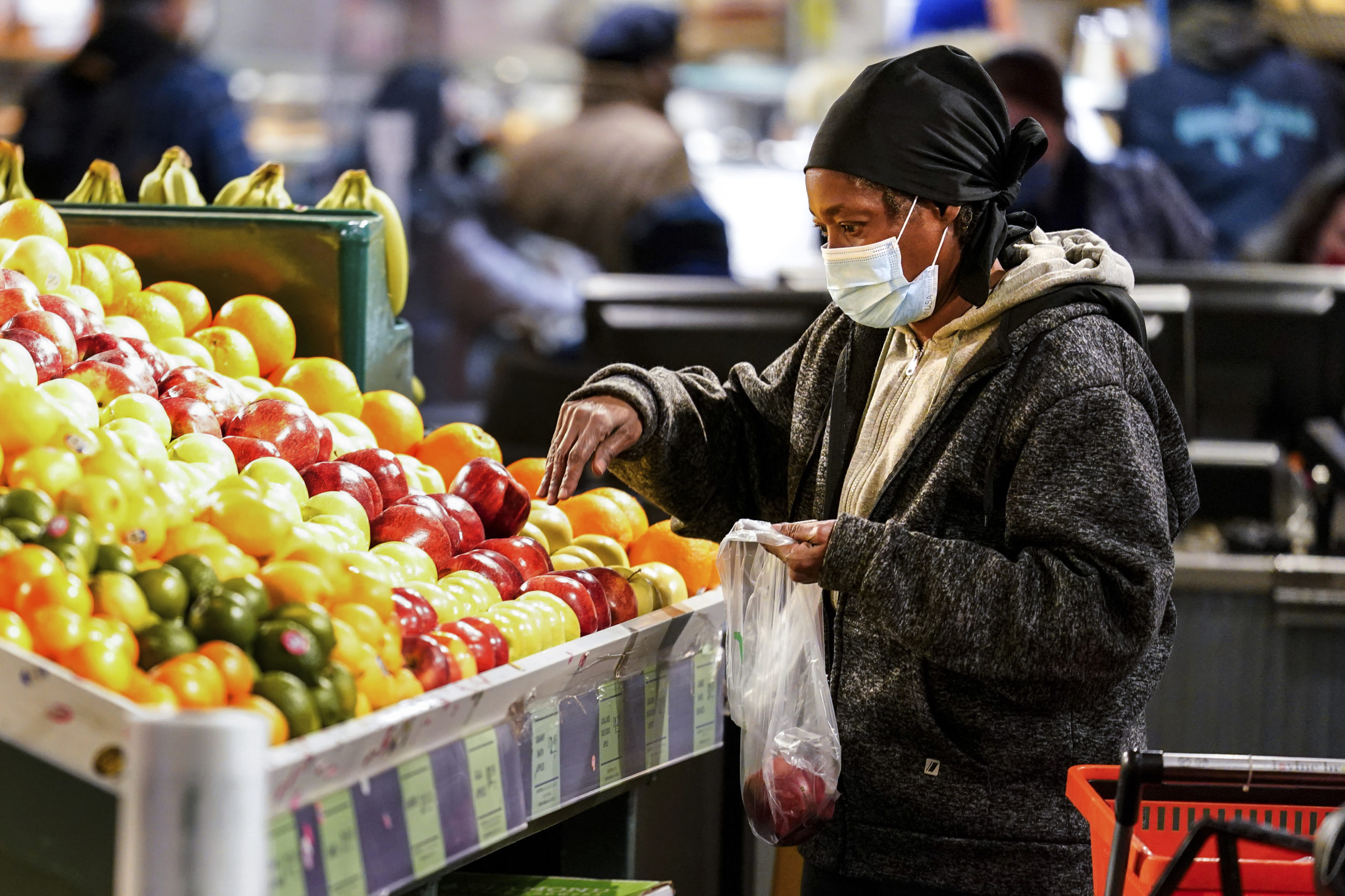 A shopper waring a proactive mask as a precaution against the spread of the coronavirus selects fru...