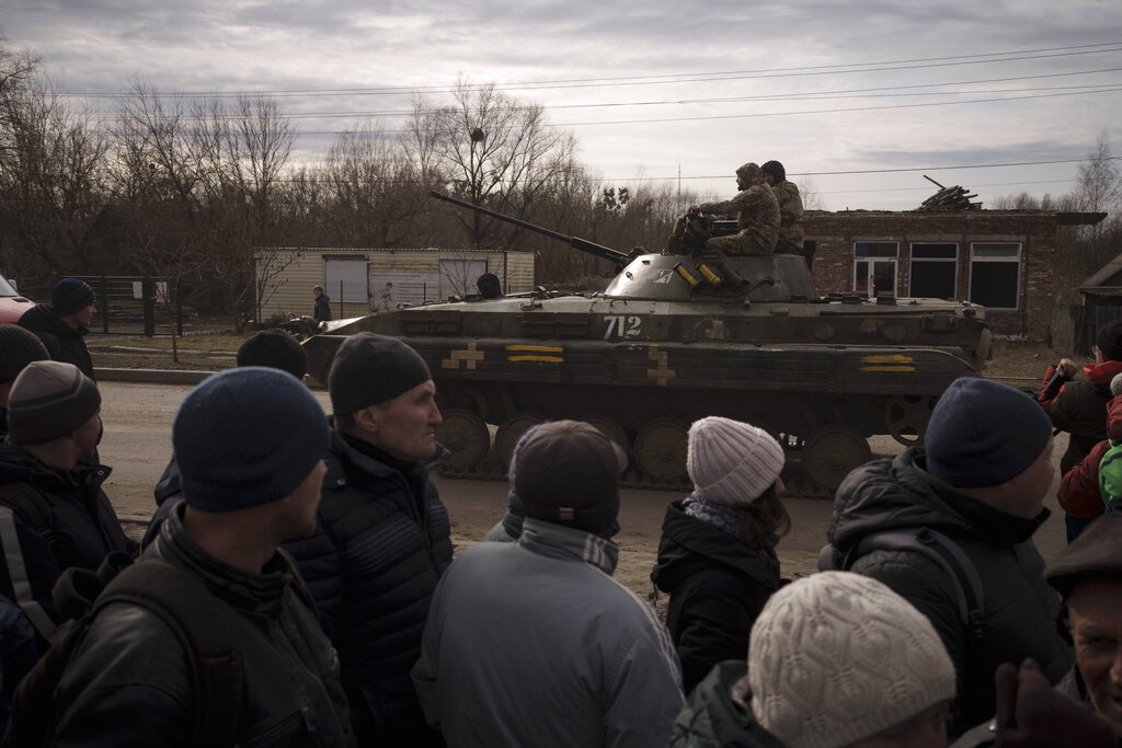 Residents lining up for aid watch as Ukrainian soldiers ride atop a tank in the town of Trostsyanet...