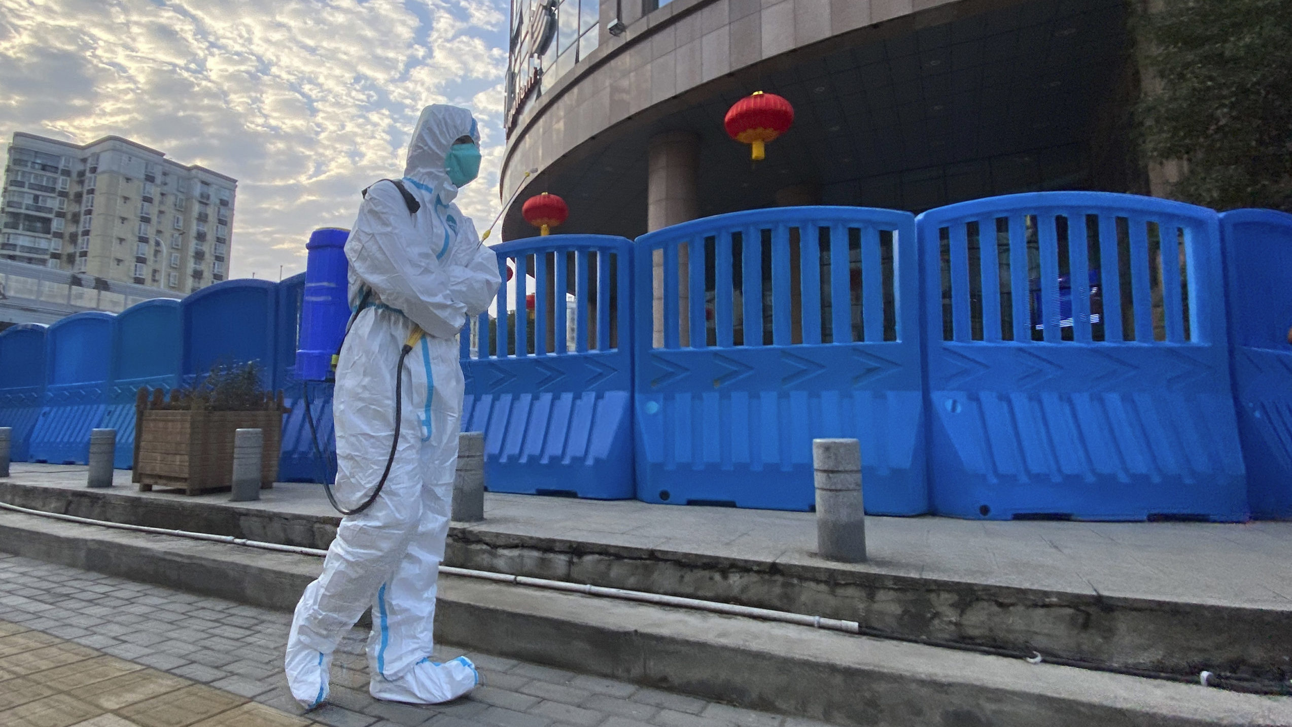 FILE - A worker in protectively overalls and carrying disinfecting equipment walks outside the Wuha...