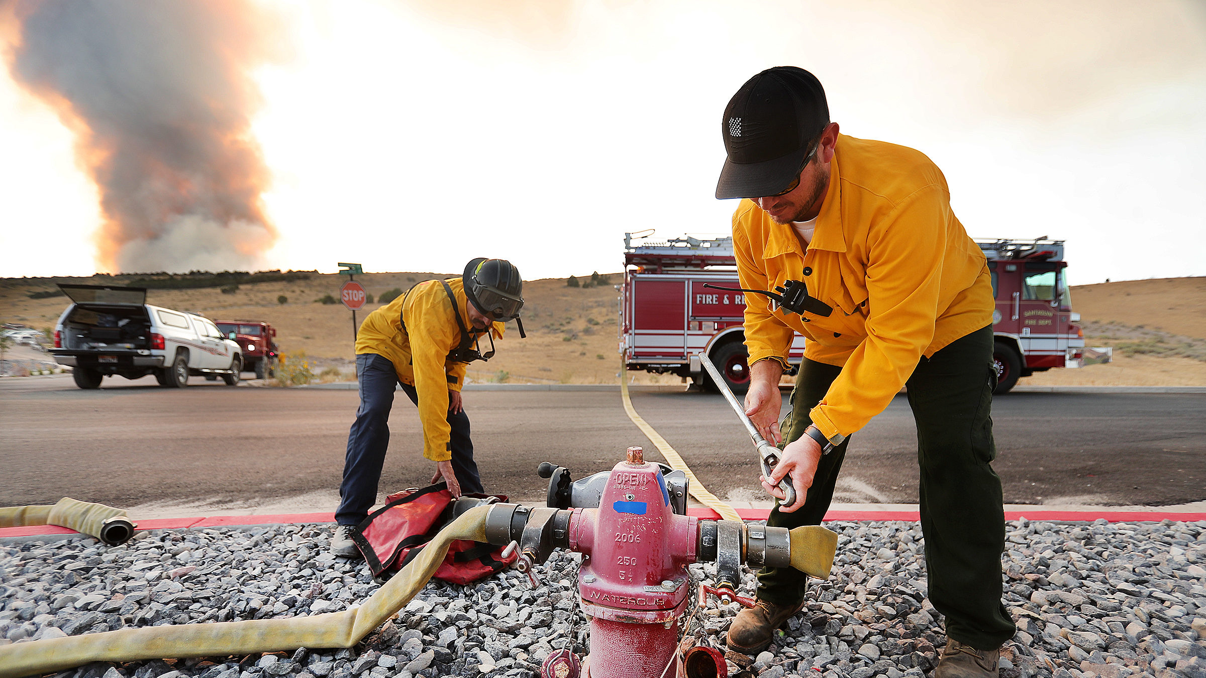 Firefighters hook up a water hose to a hydrant as crews respond to a fire burning near Goshen and S...
