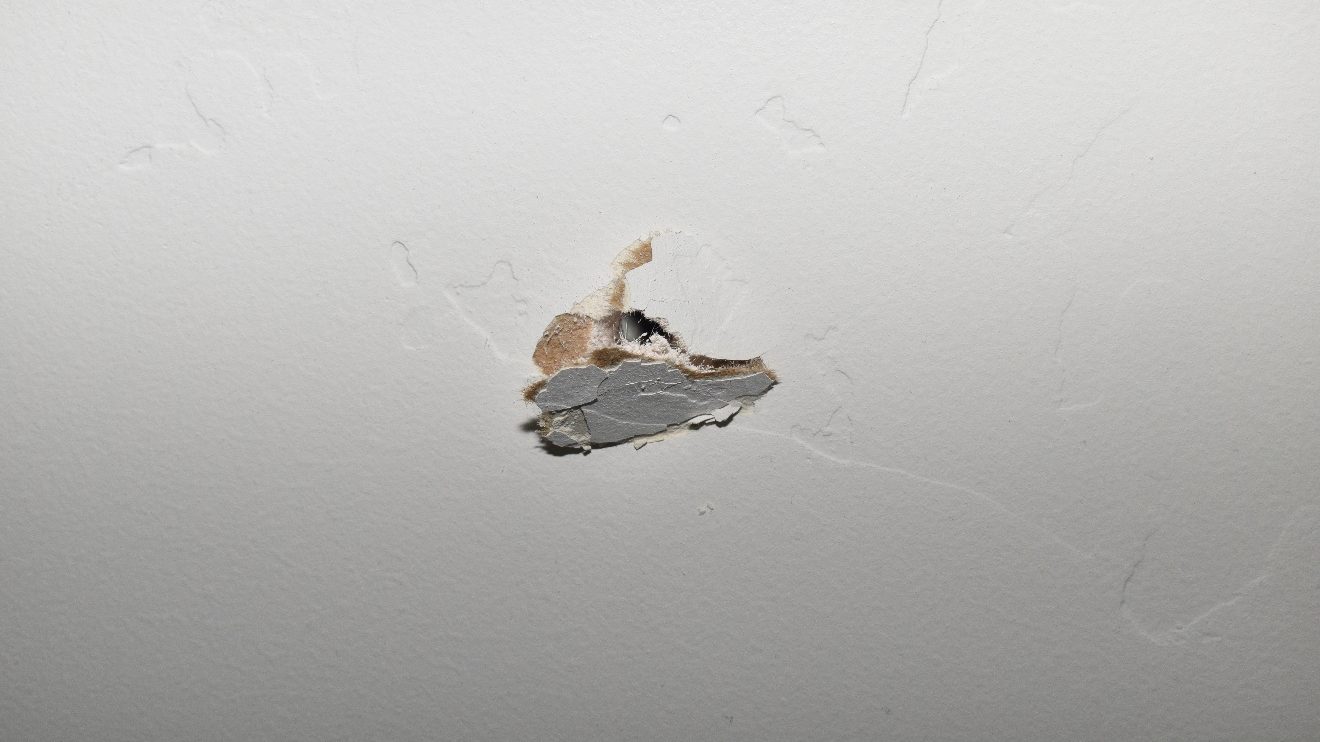 A bullet hole in a white wall. The SLCPD urges gun safety practices...