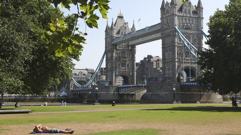 A man shields his eyes from the sun as he sunbathes backdropped by Tower Bridge in London, Tuesday ...