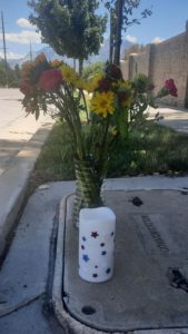 A vase with flowers and a candle sit on the street.