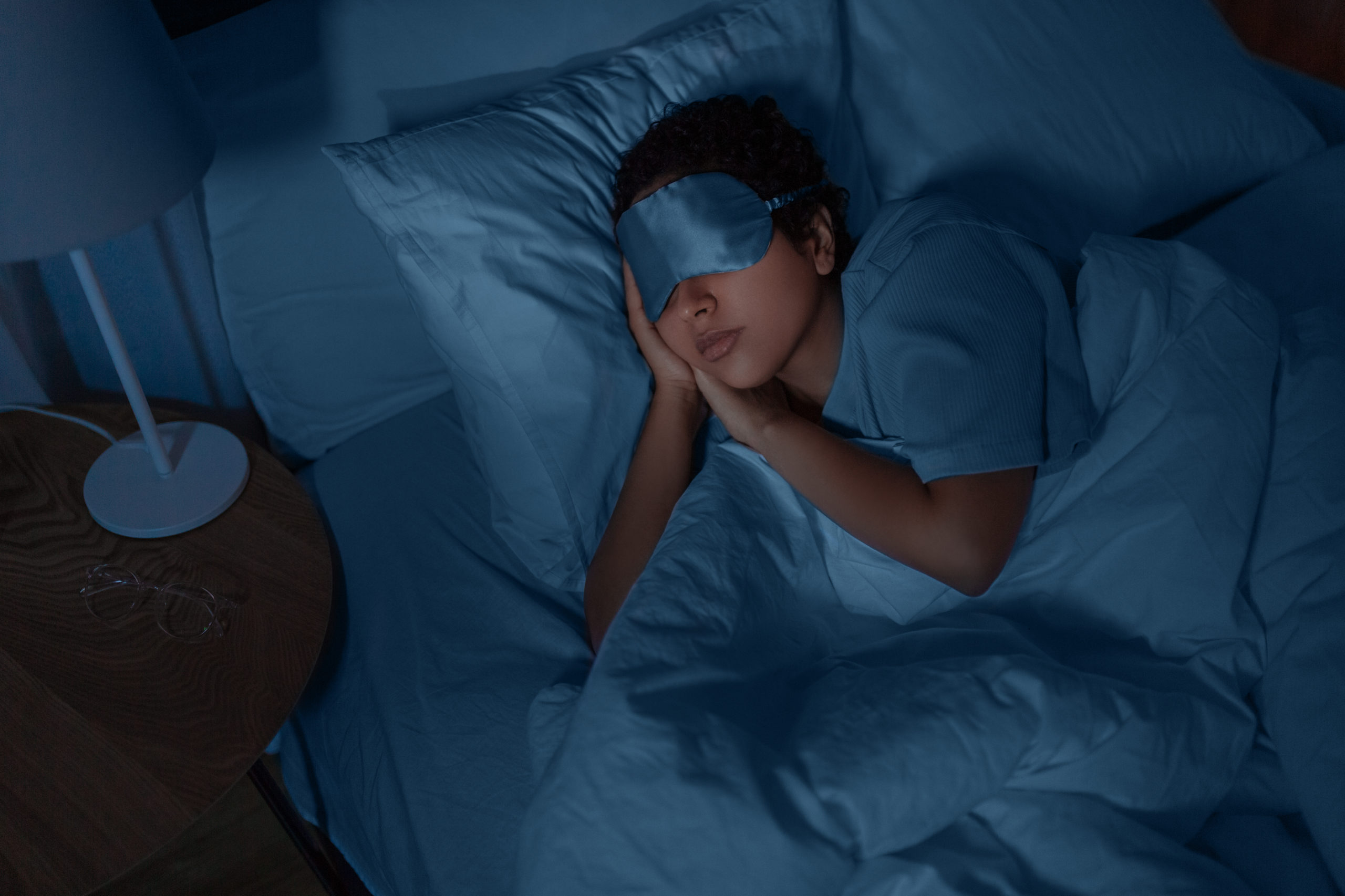people, relax and comfort concept - young african american woman in eye mask sleeping in bed at hom...