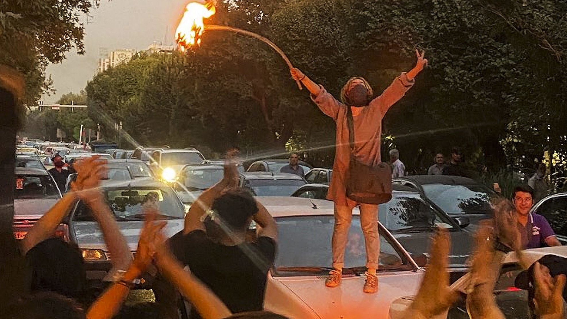 An Iranian woman on top of a car bonnet sets her headscarf on fire in central Tehran during protest...