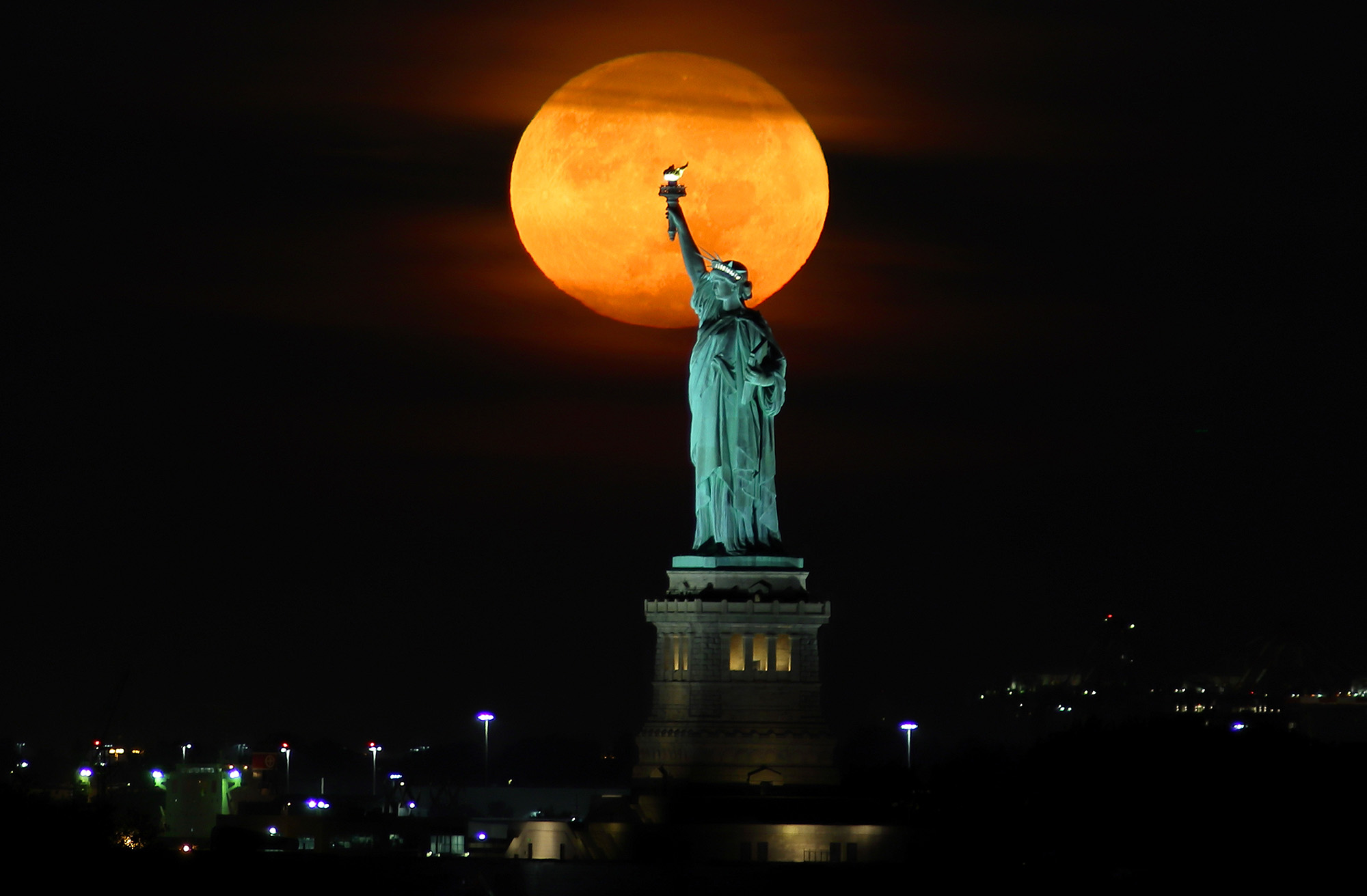 NEW YORK, NY - SEPTEMBER 20: The Harvest Moon sets behind the Statue of Liberty before sunrise on S...