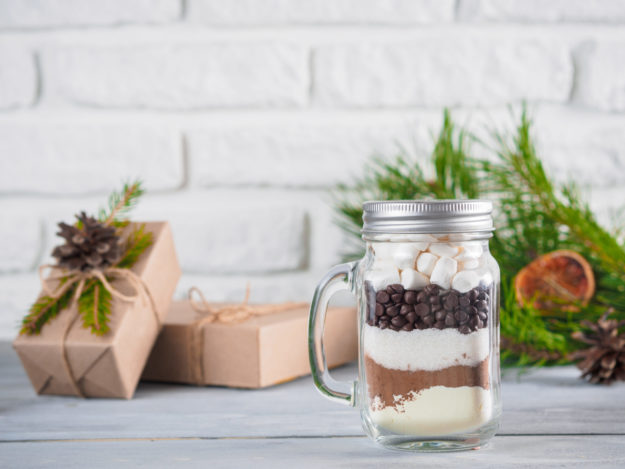 Hot chocolate mix in mason jar and rustic gift boxes on gray table and white brick wall.